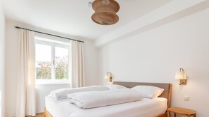 A bedroom with a wooden bed, white bedding, a small bedside table, and a window with curtains.