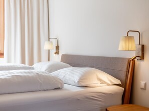 Habitación de hotel con dos camas, cabecero de madera, lámpara de pared y ventana con cortinas.