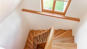 Una escalera de madera con barandilla que lleva a un rellano con ventana con vista a un jardín verde.