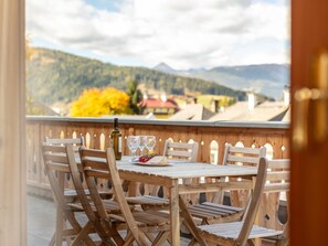 Una mesa de madera con sillas en un balcón con vistas a un paisaje montañoso.