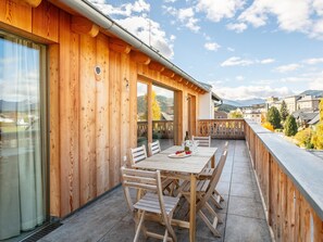 Una terraza de madera con una mesa y sillas, con vistas a un paisaje montañoso.