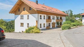 Ein zweistöckiges Gebäude mit rotem Ziegeldach, hölzernen Balkonen und einer gepflasterten Auffahrt.