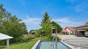 Ein Schwimmbecken mit Steinrand, umgeben von Grün und blauem Himmel.