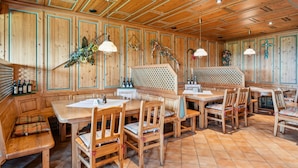 Ein Holzinterieur mit einem langen Tisch, Bänken, einer verzierten Wand und hängenden Dekorationen.