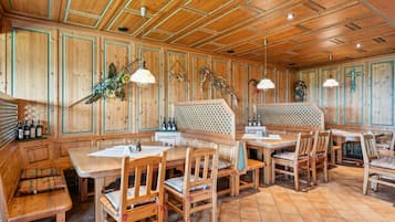 Ein Holzinterieur mit einem langen Tisch, Bänken, einer verzierten Wand und hängenden Dekorationen.