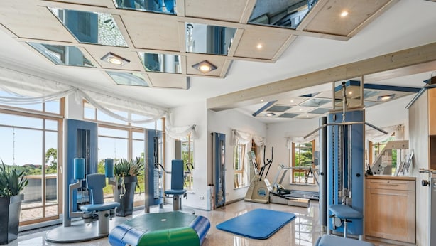 Ein geräumiger Fitnessraum mit Trainingsgeräten, großen Fenstern und Blick ins Freie.