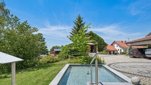 A swimming pool with a stone edge, surrounded by greenery and a clear sky. - Holiday apartment in the Bavarian Forest (Waldkirchen)
