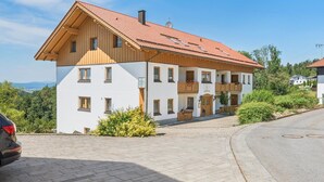 A two-story building with a red-tiled roof, wooden balconies, and a paved driveway. - Holiday apartment in the Bavarian Forest (Waldkirchen)