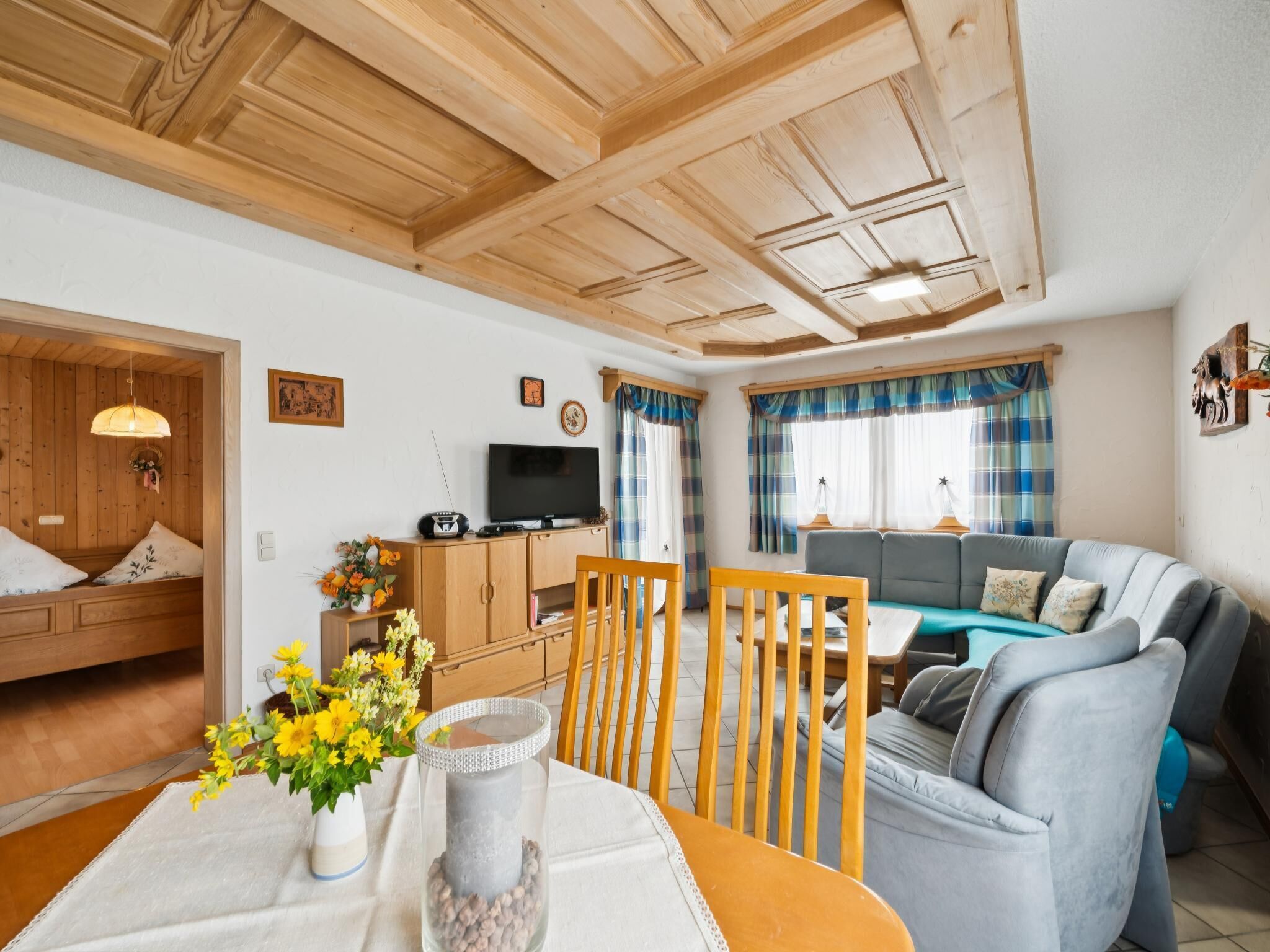 Ein gemütliches Wohnzimmer mit einer Couch, einem Esstisch mit Stühlen, einem Fernseher und einer Holzzieldecke.