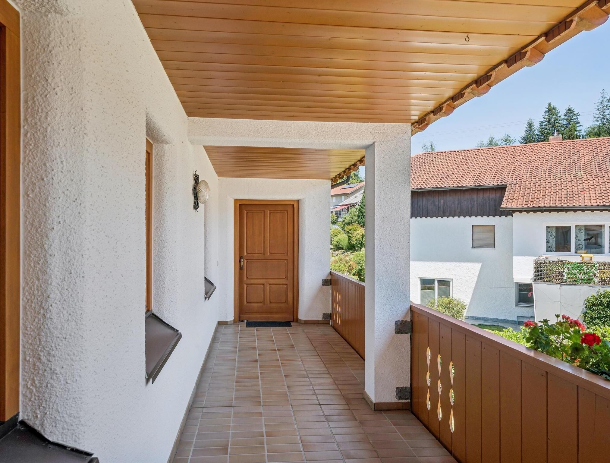 A covered balcony with a wooden door, white walls, and a tiled floor.