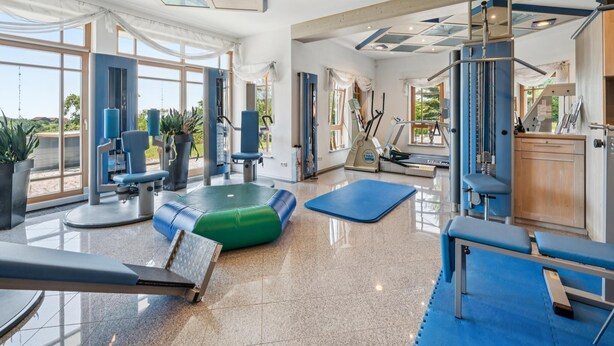 Un gimnasio amplio con equipo de ejercicio, ventanas grandes y un techo alto.