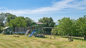 Un parque infantil con un tobogán, columpios y un pequeño refugio.