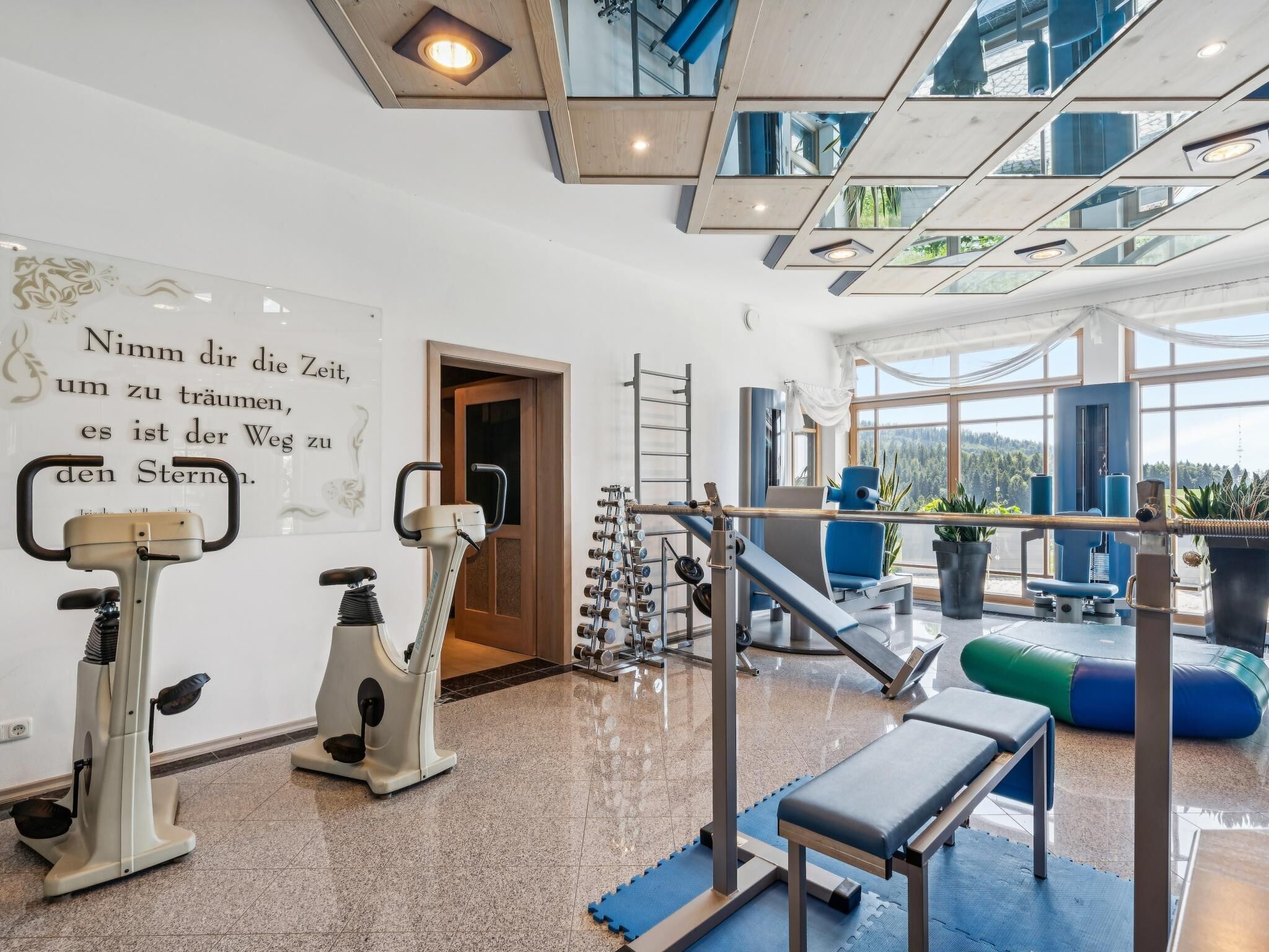Ein Fitnessraum mit Trainingsgeräten, einer Bank und einem motivierenden Spruch an der Wand.