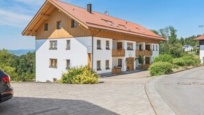 A two-story building with a red-tiled roof, a balcony, and a view of the surrounding landscape. - Quiet holiday apartment in the Bavarian Forest (Waldkirchen)