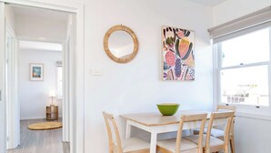 En matplats med ett träbord och stolar, en grön skål, en vävd spegel och en färgstark, abstrakt målning på väggen.