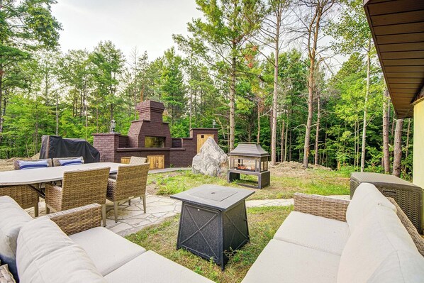 An outdoor patio with wicker furniture, a stone fire pit, and a brick grill area surrounded by trees. - Privacy Magical Forest Cottage 30+ Party Room,  Disco KTV (Uxbridge)