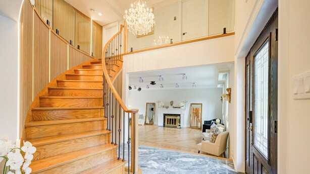 A spacious living area with a wooden staircase, a chandelier, and a fireplace.