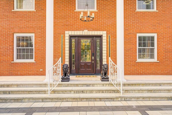 A brick building with a dark wooden door, two lion statues on the steps, and a white railing. - Privacy Magical Forest Cottage 30+ Party Room,  Disco KTV (Uxbridge)