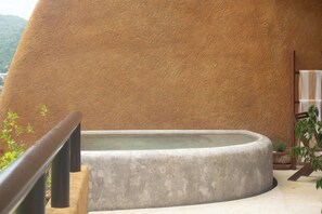 A spa area with a large stone wall, a hot tub, and a wooden railing.