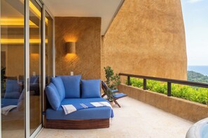 A balcony with a sofa, a potted plant, and a view of the ocean.