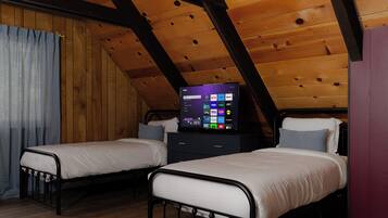 A room with two beds, a television on a dresser, wooden ceiling beams, and a curtain.