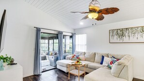 Uma sala de estar moderna com um ventilador de teto, um conjunto de sofá, uma mesa de centro com frutas e vista através da porta de vidro.