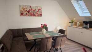 A dining area with a table, chairs, a vase with flowers, a painting on the wall, and a kitchen area with a coffee machine. - Spacious Apartment with Lake View, Shared Terrace and Wi-Fi (Feldberger Seenlandschaft)