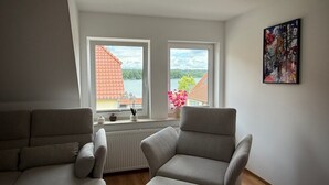A room with two grey armchairs, a radiator, and a window with a view of a red-roofed building and greenery. - Spacious Apartment with Lake View, Shared Terrace and Wi-Fi (Feldberger Seenlandschaft)