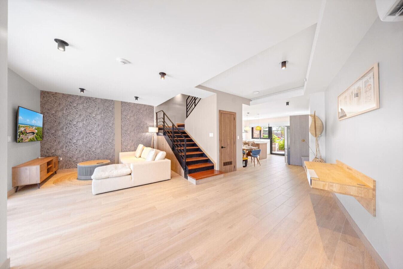Een ruime woonkamer met houten vloer, een trap, een bank en een eethoek.