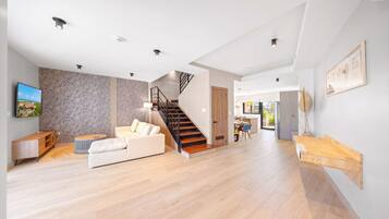 Een ruime woonkamer met houten vloer, een trap, een bank en een eethoek.