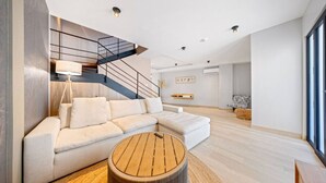 Un salon moderne avec un canapé d’angle, une table basse ronde en bois et un escalier doté d’une rampe en métal.