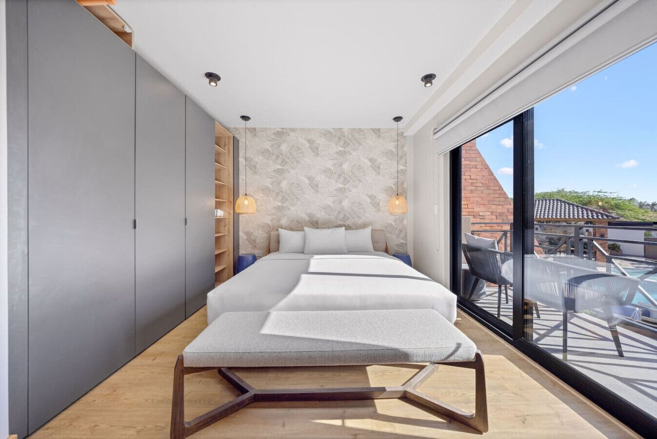 A modern bedroom with a large bed, a wardrobe, and a view of a pool and outdoor area.