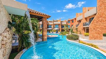 A swimming pool with a waterfall feature, surrounded by multi-story buildings with balconies and outdoor seating.