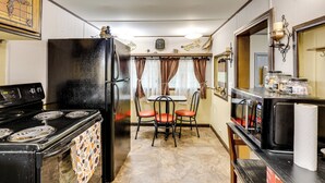 A compact kitchen with a stove, refrigerator, and microwave. There is a dining table with chairs and a window with curtains. - No Pet Fee! Peaceful Escape at Towner Properties (Langston)