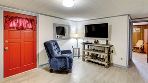 A room with a red door, a blue armchair, a TV, a lamp, and a wooden shelf. - No Pet Fee! Peaceful Escape at Towner Properties (Langston)