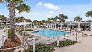 A pool area with lounge chairs, palm trees, and a clear sky.