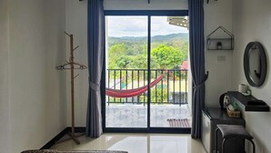 Una habitación con cama, escritorio, silla, hamaca y un balcón con vista a follaje.