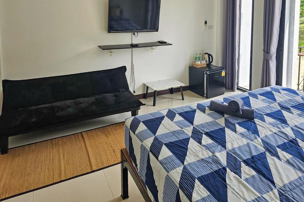 A hotel room with a bed, a sofa, a television, a small table, a refrigerator, and a window with curtains.