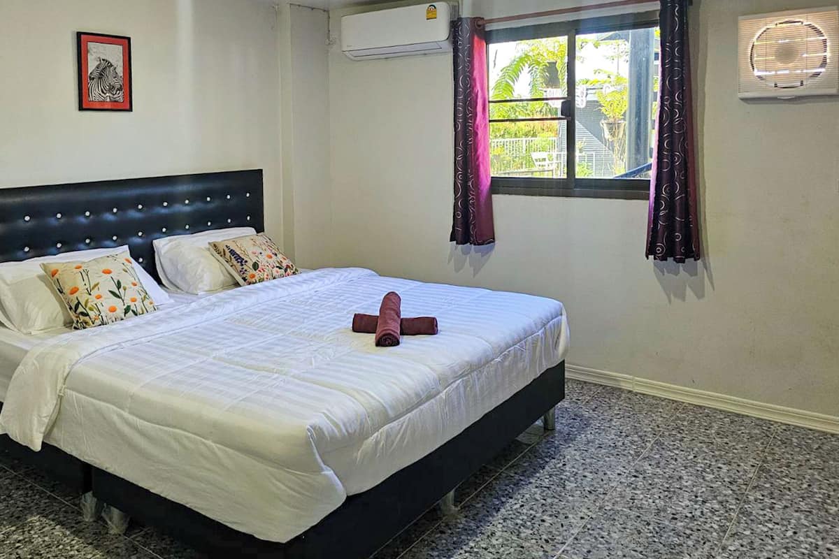 A neatly made bed with a striped bedspread, two pillows with floral patterns, and a rolled towel on the bed.
