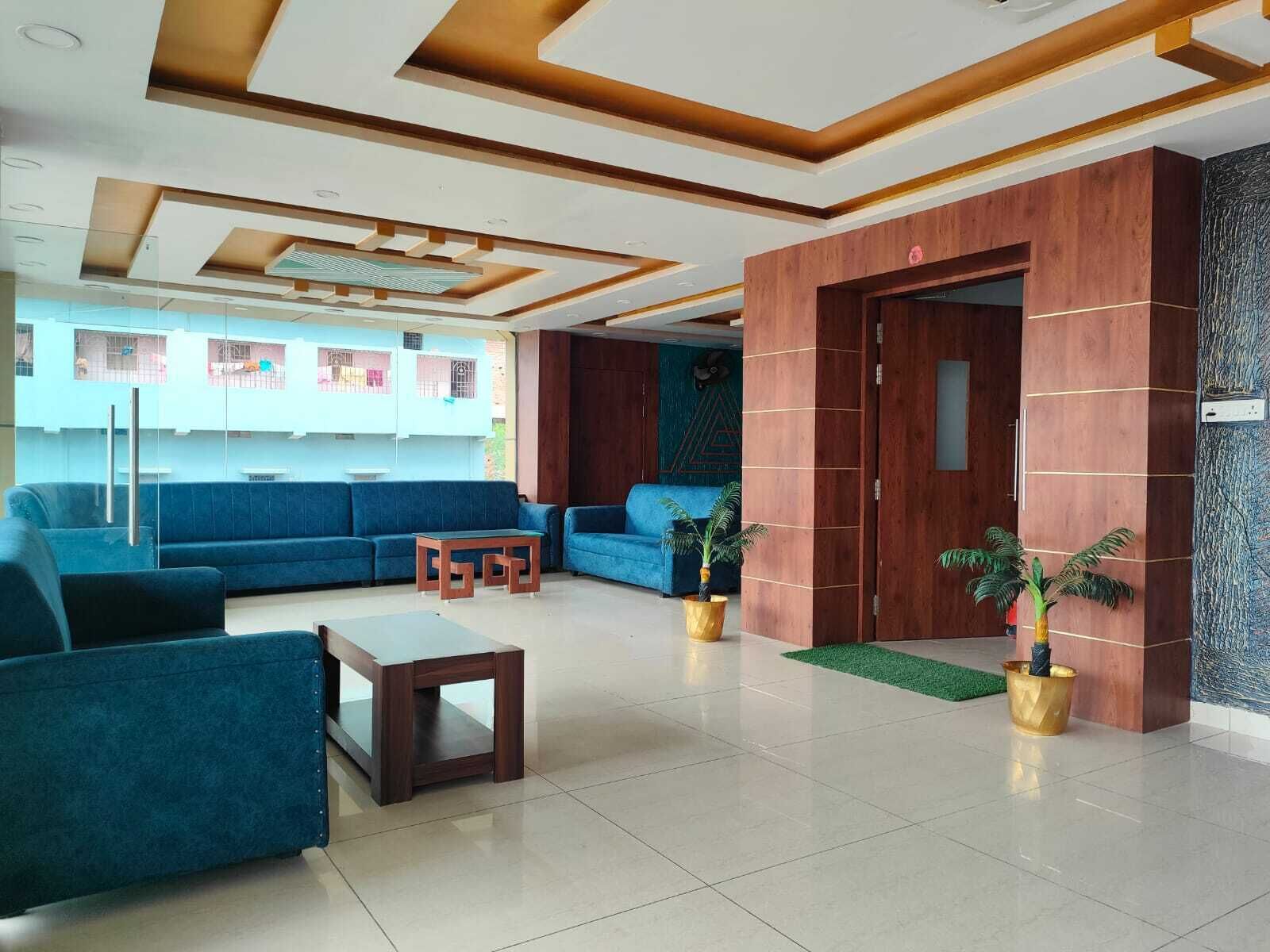 A modern lobby with blue sofas, a wooden reception desk, and a large wooden door.