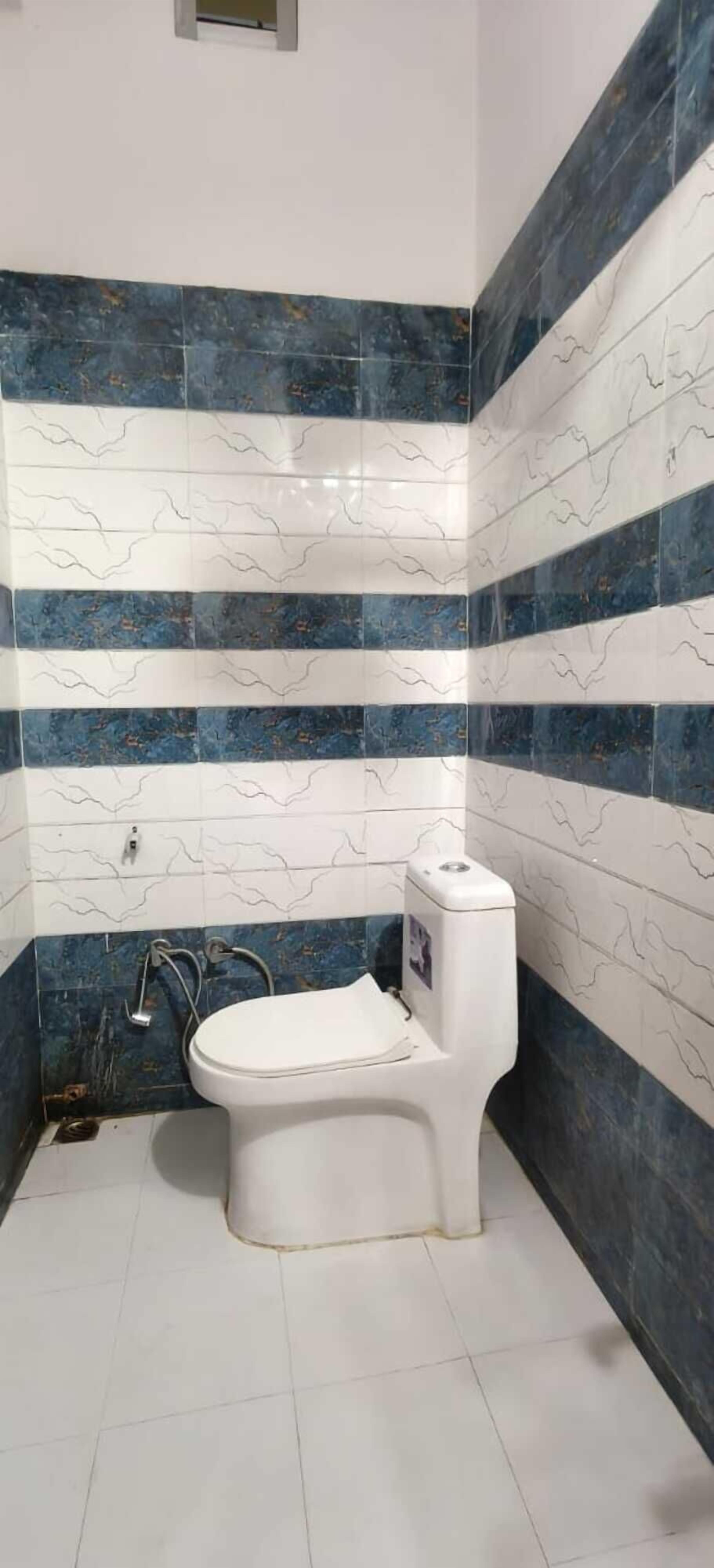 A bathroom with a toilet, a hand dryer, and a wall-mounted faucet. The walls are tiled with a blue and white pattern.