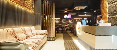 A hotel reception area with a sofa, a reception desk, and a television screen.