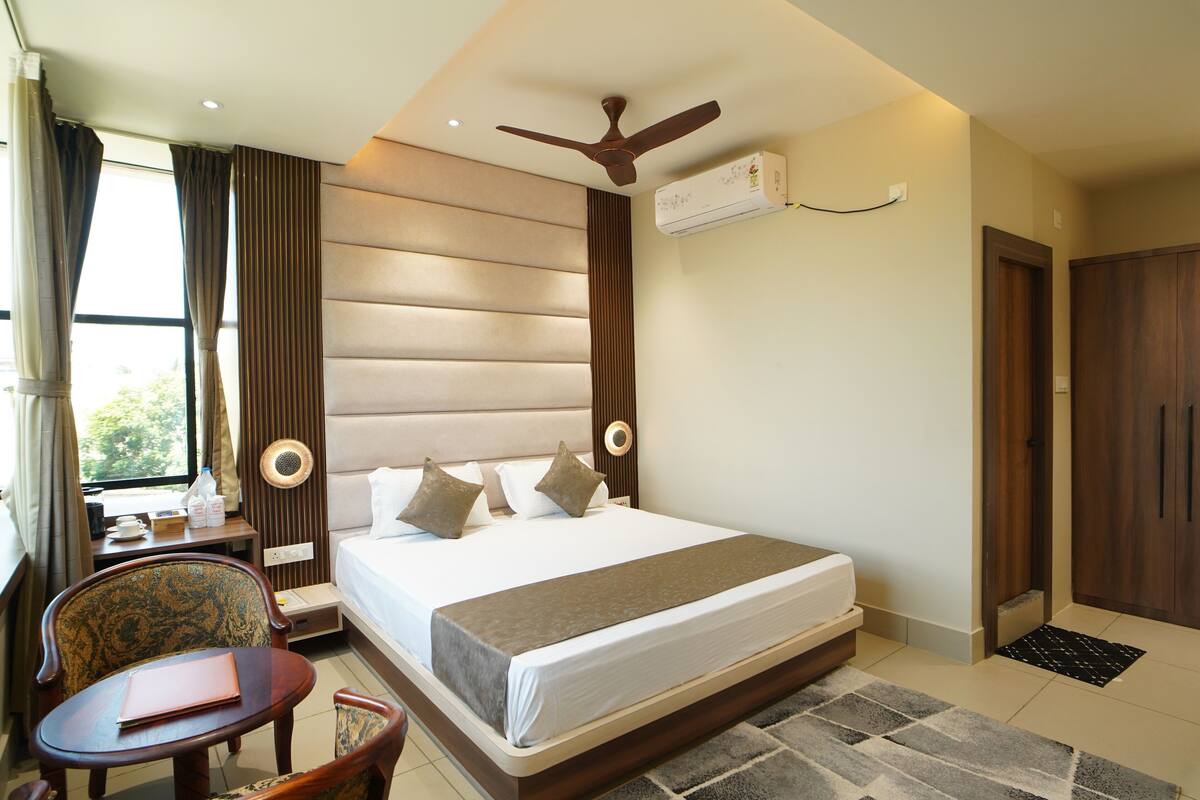 A hotel room with a large bed, a desk with a chair, a ceiling fan, and an air conditioning unit.