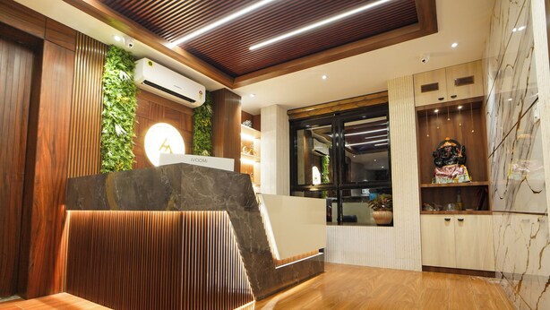 A reception area with a wooden reception desk, a green vertical garden, marble flooring, and a marble wall.