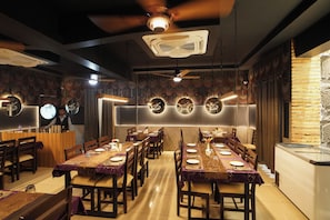 Ein Restaurant mit mehreren Esstischen, Deckenventilatoren und dekorativer Wandbeleuchtung.