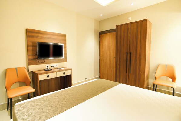 A hotel room with a bed, a TV mounted on the wall, a wooden wardrobe, and two orange chairs. - Hotel Atithi (Bhadrak)