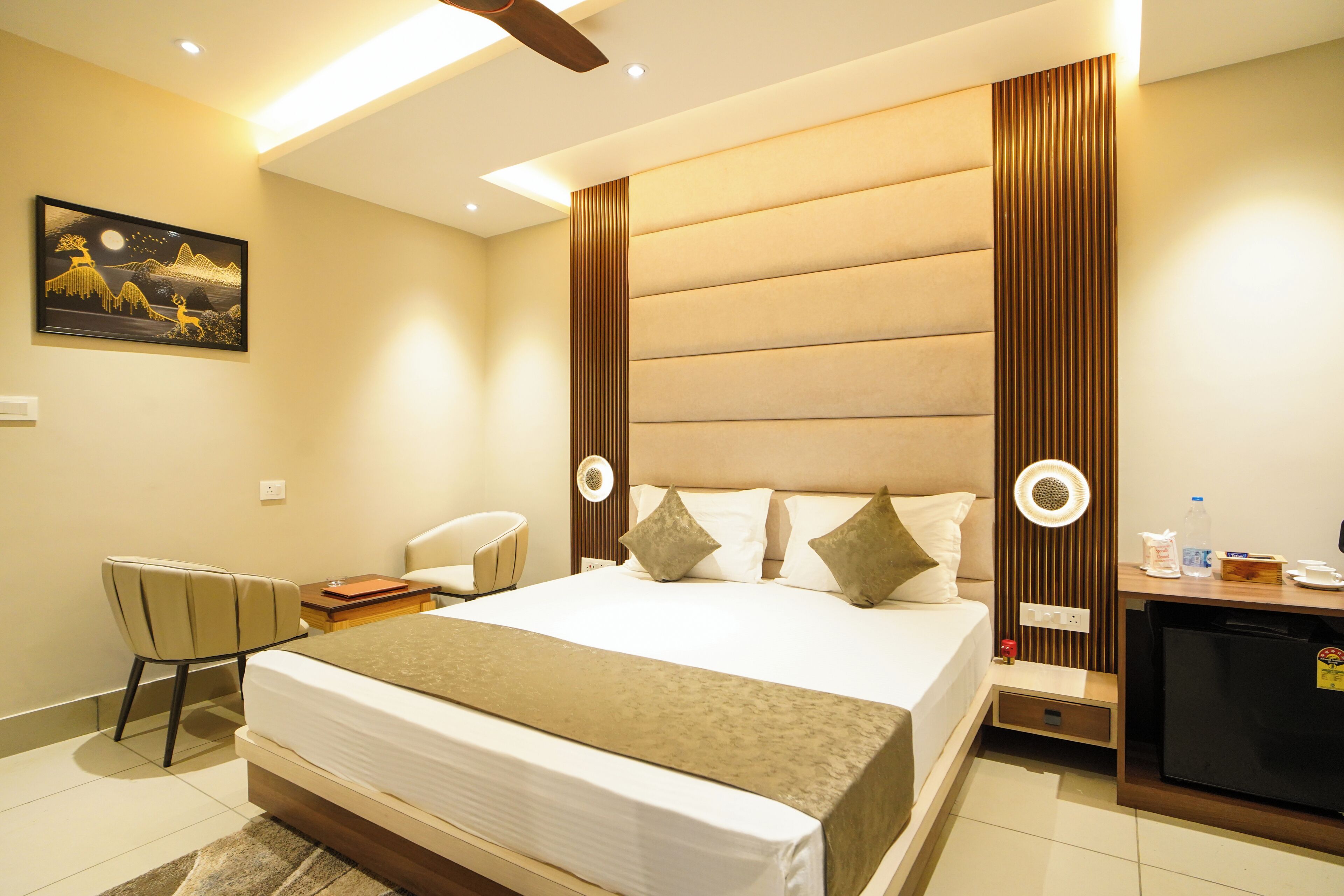 A hotel room with a large bed, a desk with a chair, a refrigerator, and a wall-mounted artwork.
