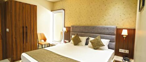A hotel room with a large bed, wooden wardrobe, a chair, and a bedside table with a lamp.