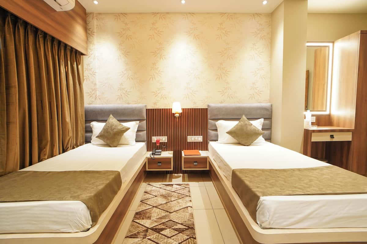 A hotel room with two beds, a wooden headboard, a patterned wall, a small desk with a lamp, and a mirror.