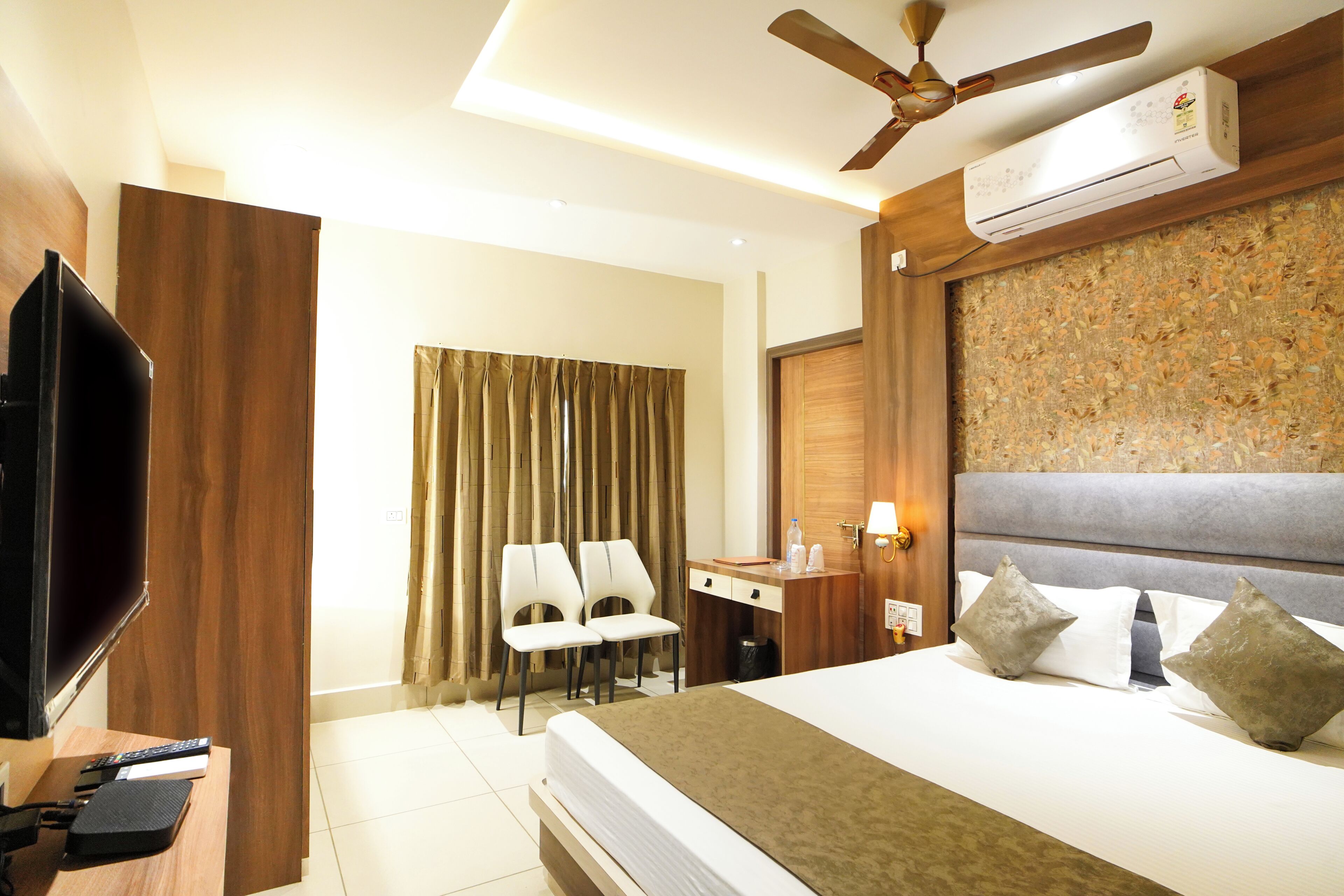 Una habitación de hotel con cama, escritorio, dos sillas, televisor y aire acondicionado.